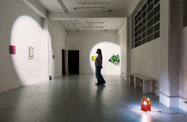 A masked woman browsing the works of art in a dimly lit gallery space.