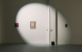 A spotlight shining on a wall of two small art works.