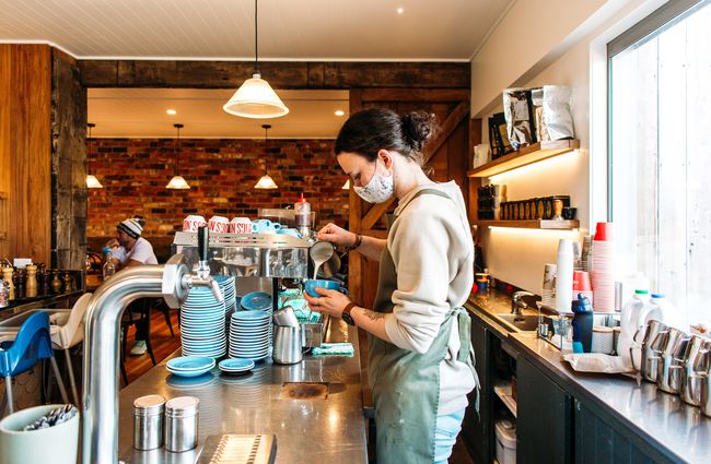 A staff member pouring milk into a coffee behind the counter at Punnet Eatery.
