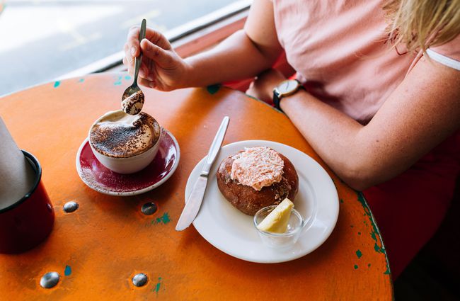 A woman with a coffee and doughnut at a table at Queen Sally's Diamond Deli and cafe Wellington.