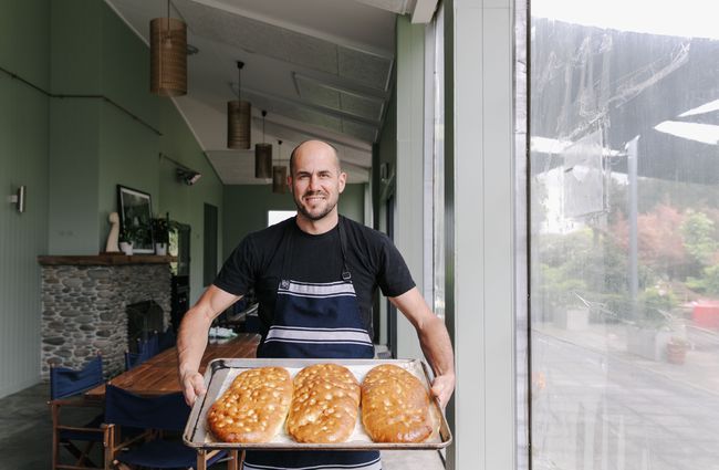 Bevan holding tray of fresh focaccia bread at Riverstone Kitchen in Waitaki.