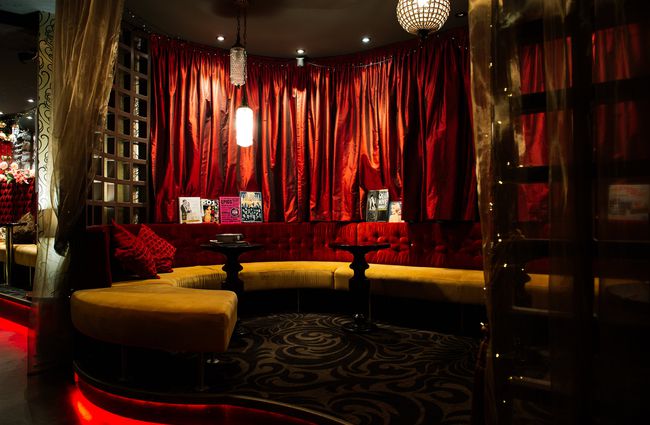 The seating area in the bar surrounded by red velvet curtains.