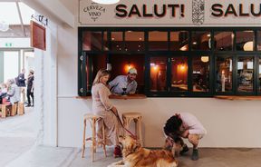 Woman drinks wine with her dog outside a tapas bar.