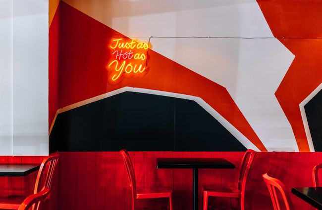 Table with a 'Just As Hot As You' neon sign above it at Soul Shack, Wellington.