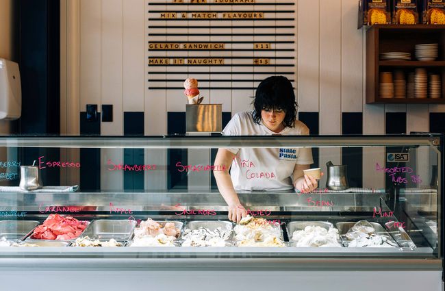 A woman behind a counter scooping gelato.