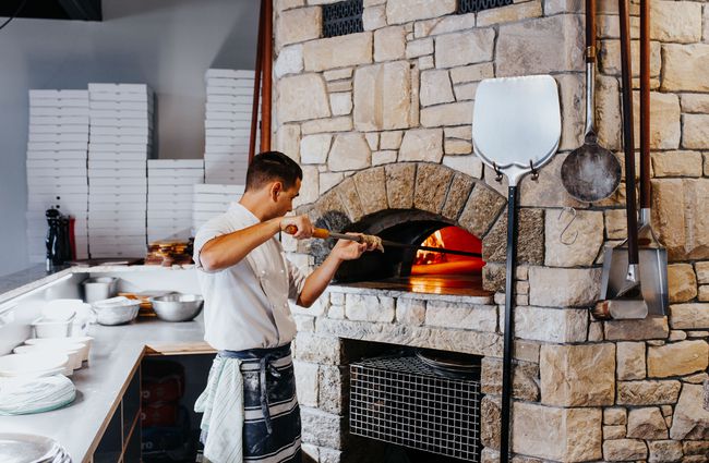 A chef putting a pizza into a wood fired oven.