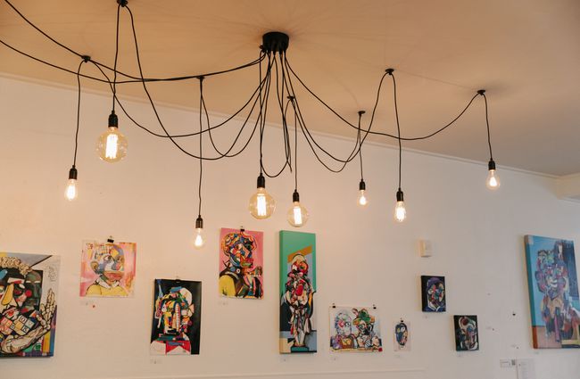 Lots of lightbulbs on hanging wire with artwork on wall behind.