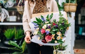 A woman holding a bright and colourful bouquet outside The Flower Crate.