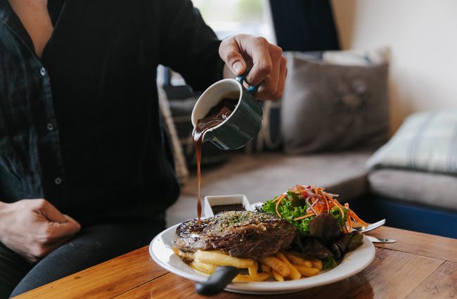 A person pouring gravy over their steak dinner at The Fort Enfield in Waitaki.