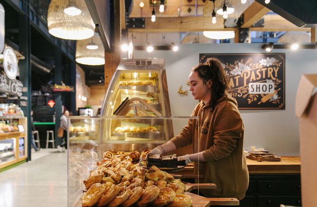 Woman putting pastries out on display.