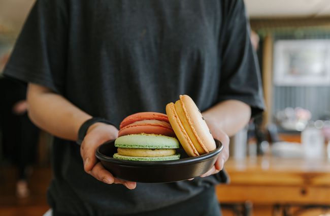 A staff member holding a plate of giant macarons at The Greedy Cow Café in Tekapo.