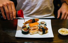 Man pouring soy sauce on a plate of sushi.