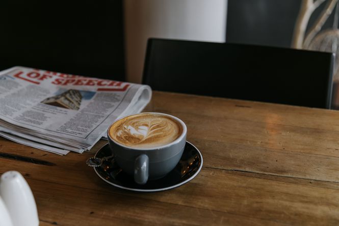 Close up of a flat white and newspaper on a table.