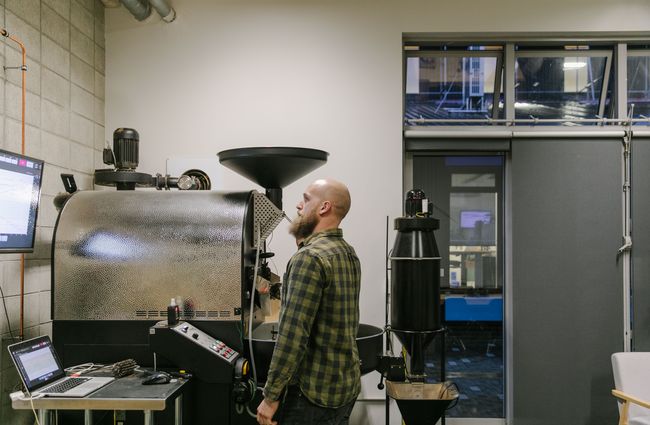 Man operating computer linked with coffee roaster.