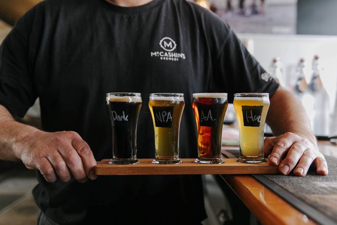A male staff member wearing a black t-shirt holding a tray of different types of beers to try at McCashin's Brewery around Stoke.