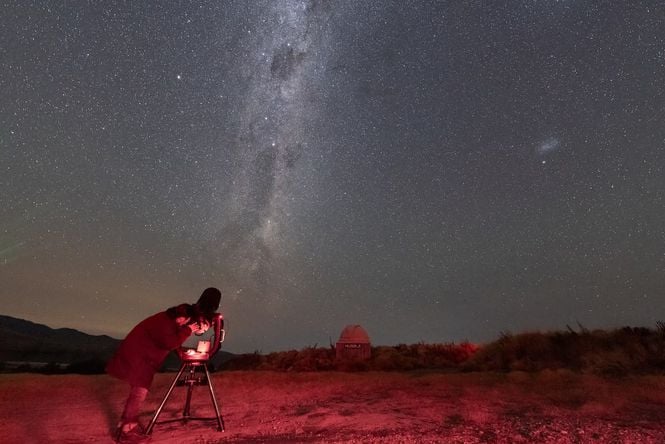 A person looking through a telescope at a star filled night sky.