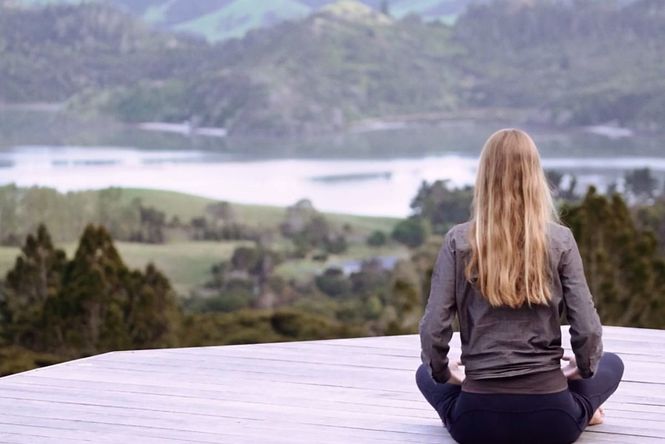 Woman sat on wooden deck doing yoga at Mana Retreat Centre.