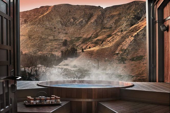 Steaming cedar-lined hot pools with wooden deck overlooking brown and green hills.