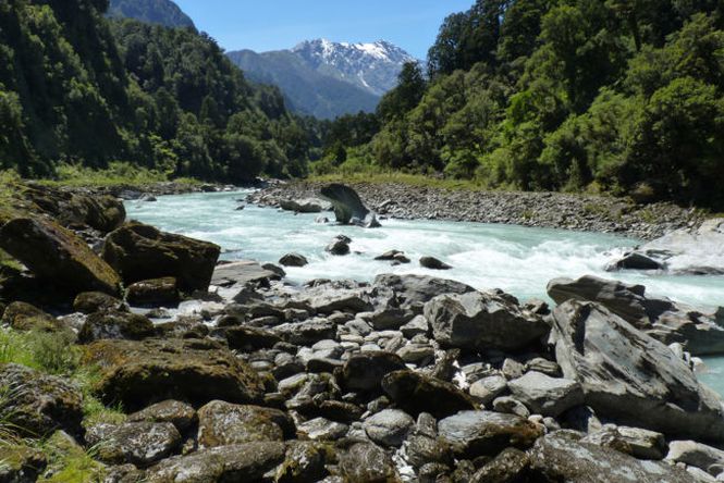 A River flows through the valley surrounded by trees and river rocks.