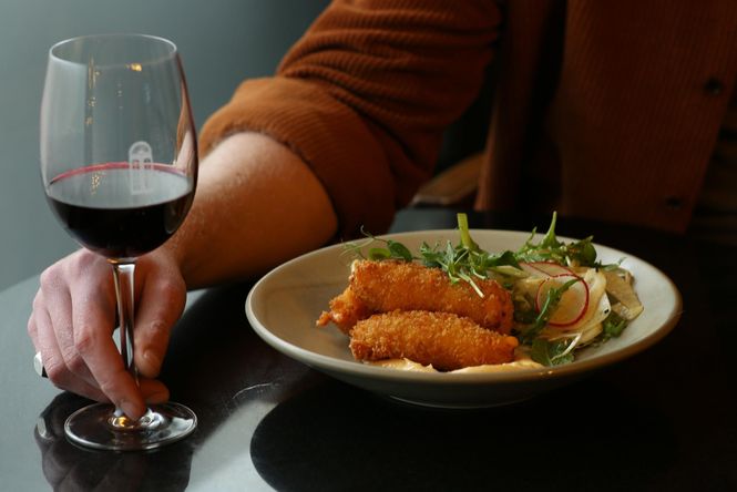 A plate of Piquant Kimchi and Gruyère Croquettes on a plate next to a glass of red wine.
