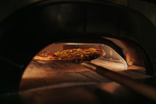 A pizza cooking inside a wood fired oven inside Pizza Trap at Space Academy bar.