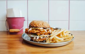 Close up of a burger and chips on table against a white tiled walled with pink grouting.