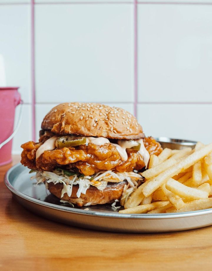 Close up of a burger and chips on table against a white tiled walled with pink grouting.