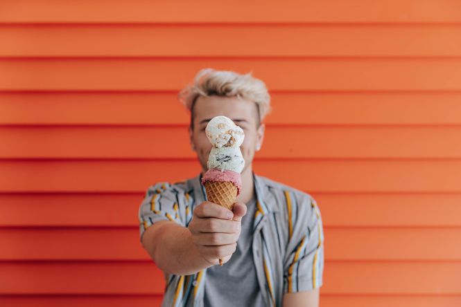 Man holding a three scoop ice cream in front of an orange wall.