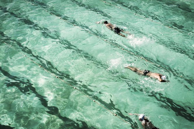 Three people swimming in an outdoor pool by Fiona Smallwood.