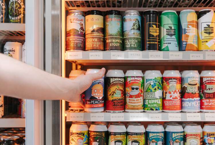 Hand reaching into fridge to grab a can of craft beer.