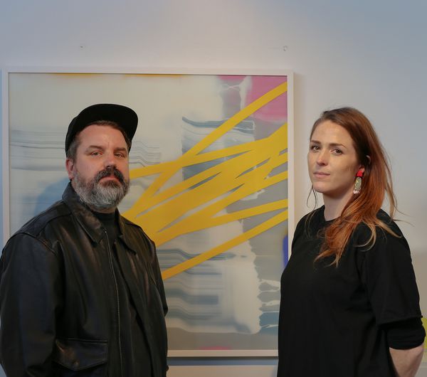 Nathan and Jen Ingram standing in front of an artwork in their gallery, Fiksate.