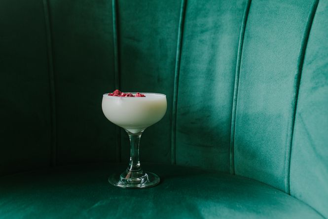 Close up of a cocktail sitting on a table in front of a velvet green couch.